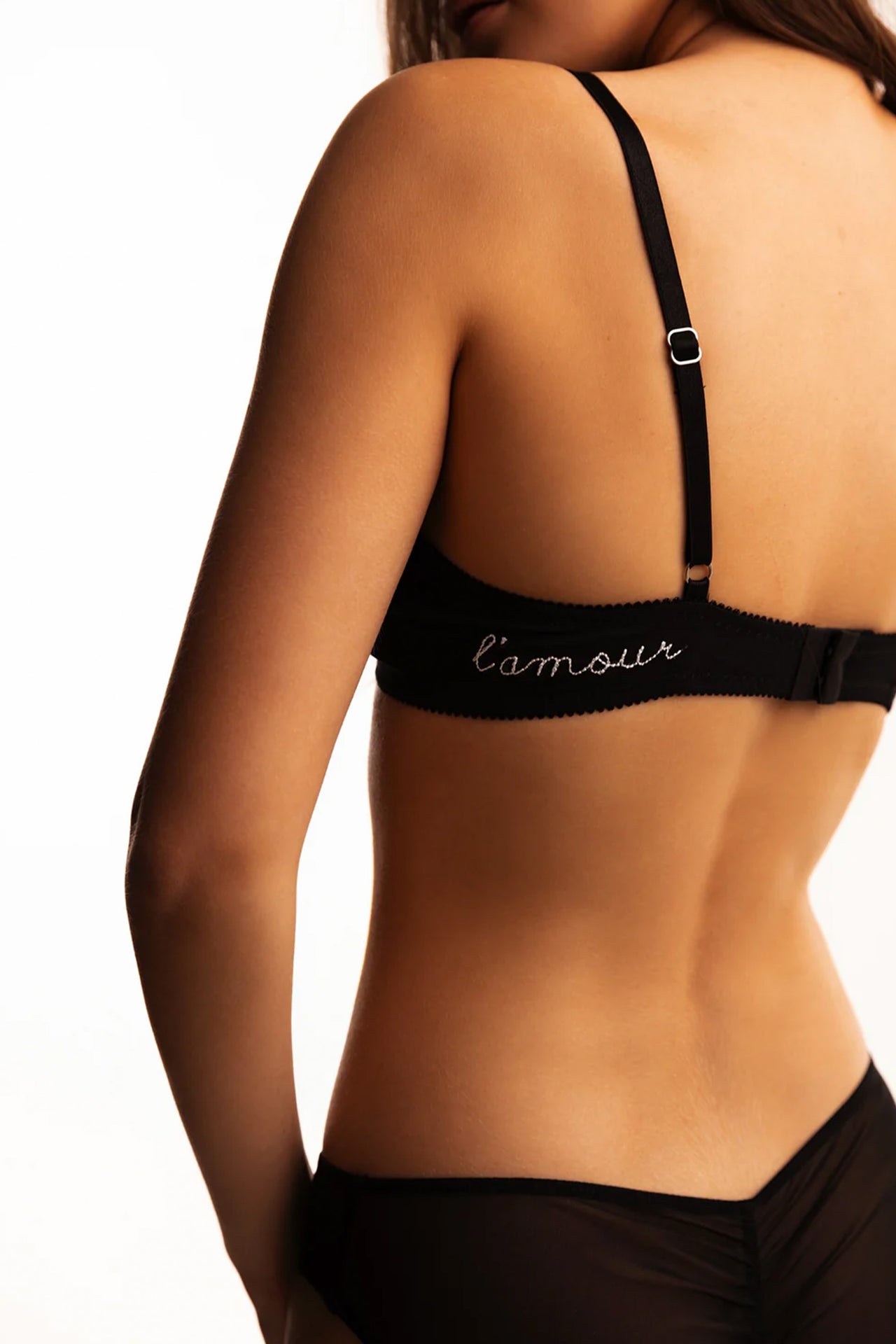 Love & Swans L'amour bralette in black mesh, frontside view on model. Plunging neckline with small red heart embroidered on side of right cup. Narrow black elastic straps.