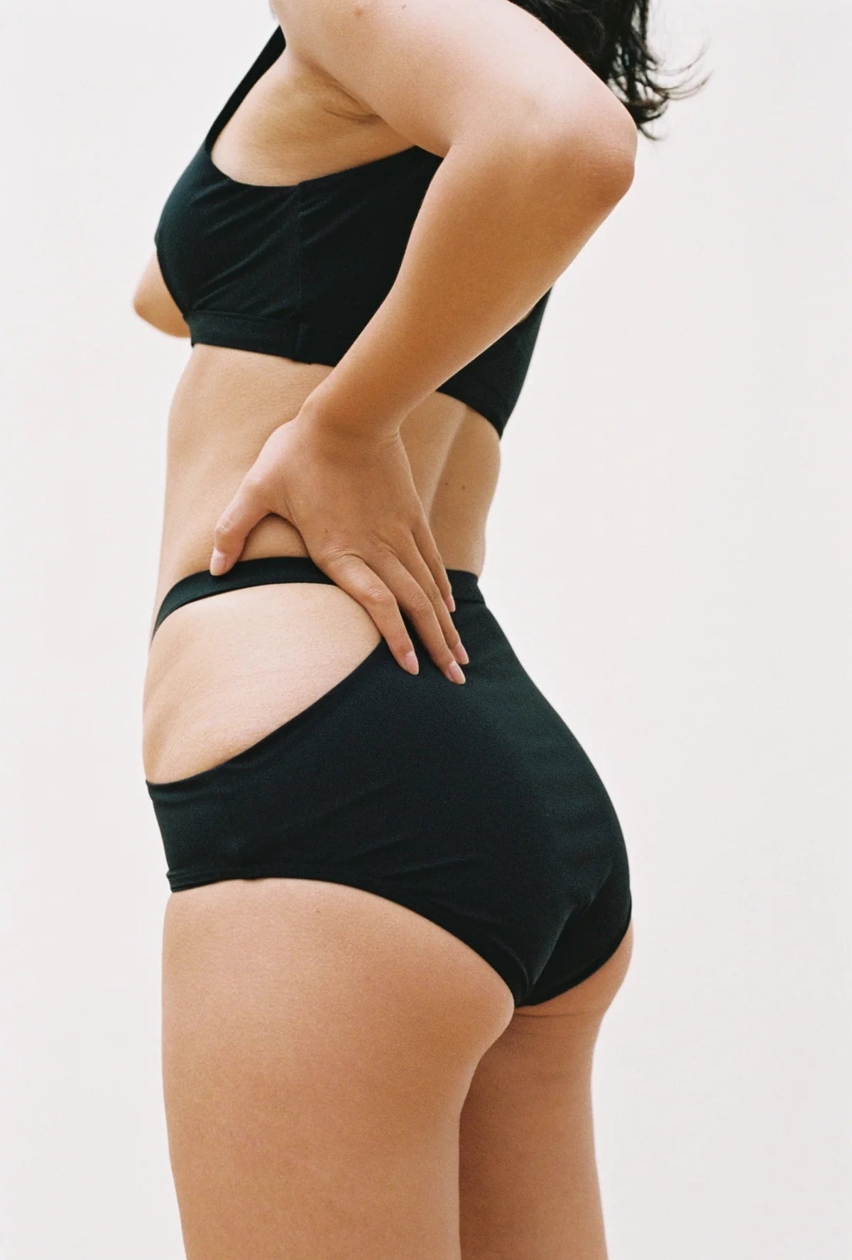 Marieyat Sade swim brief in black, high waisted with hip cut out. Double exposure photo showing side view and front on model.