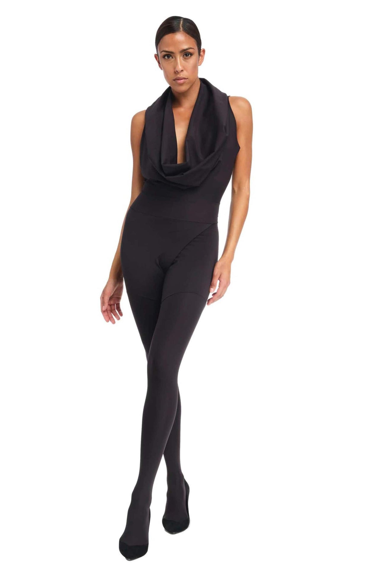 Footed, sleeveless black shadow suit by DSTM with cowl neckline and hood draped on top of the model's head. Front view on model who is taking a step forward.