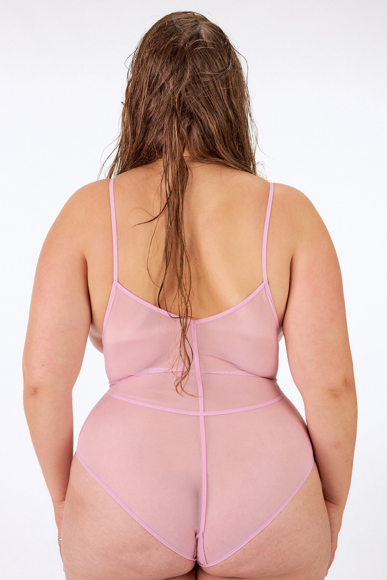 Above bodysuit in pink rose by La Fille d'O. Front view on model shows the reverse side, making the body suit cupless with cutout at the stomach and thin straps across the chest.