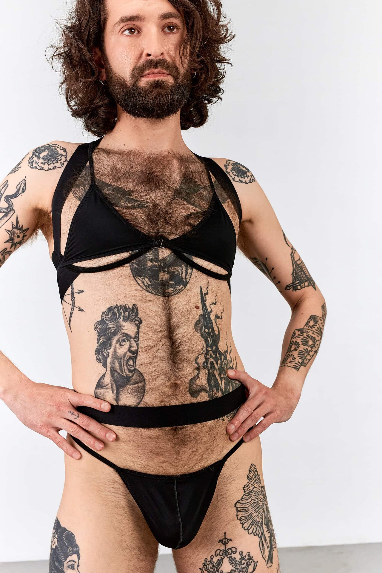 La Fille d'O Seventeen bottom cup thong, front view on model. Image shows wide elastic waistband and thin elastic hip straps. Model is also wearing open cup Night Shift bra layered with a simple triangle bralette.