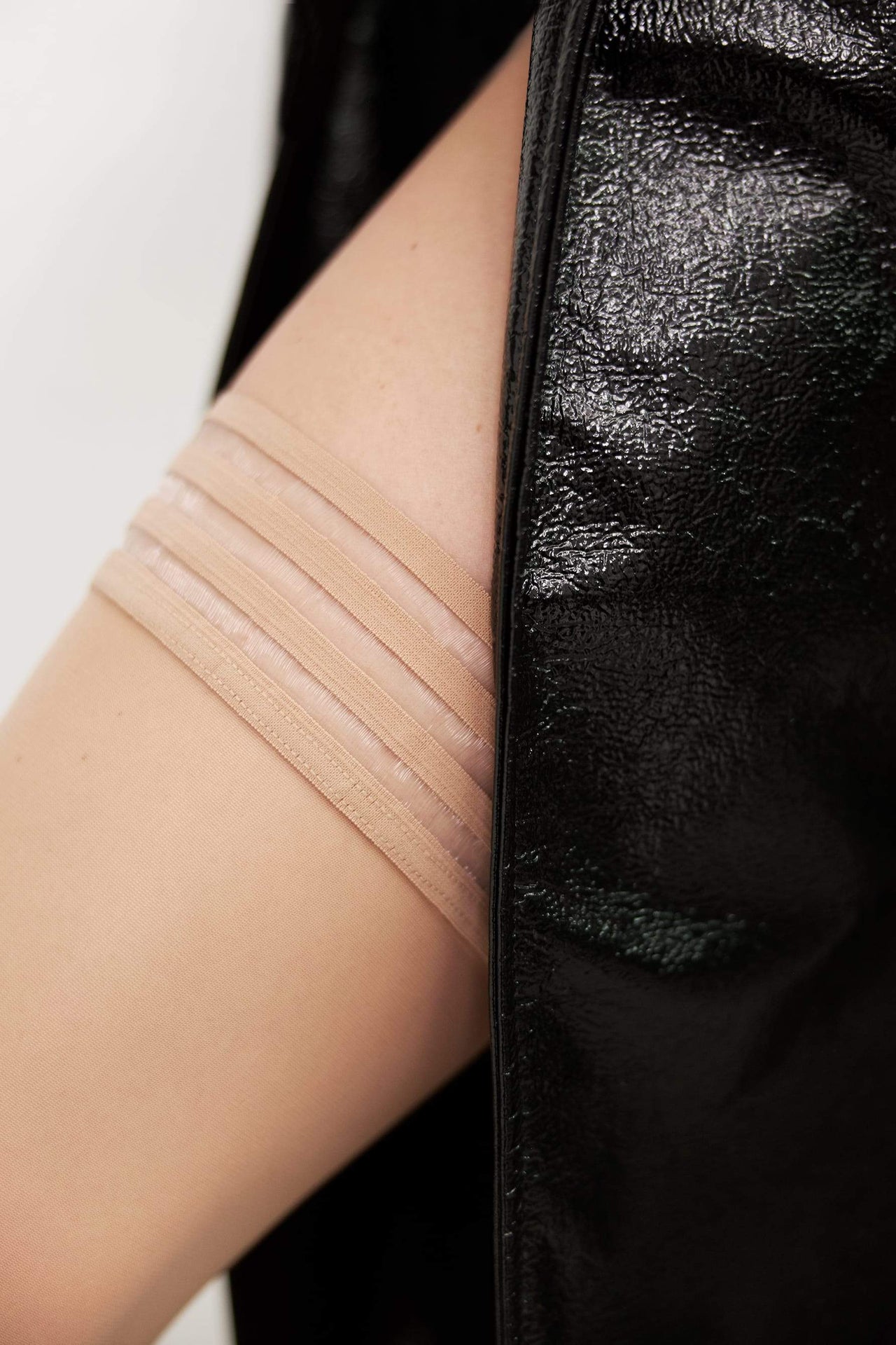 Swedish Stockings Mira stay up thigh high stockings in beige sand. Welt has beige & clear stripe pattern. Shown on model with leg protruding from black leather coat.