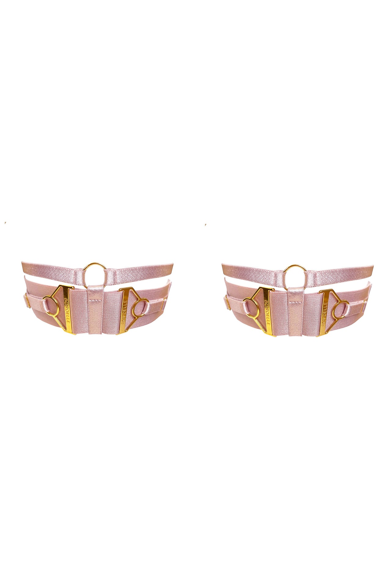 Bordelle Retta garters in rose pink with gold hardware. Thin upper straps with wider lower strap that has a thin strap on top of it attached by triangular branded hardware pieces. Upper and lower straps are joined by a gold O-ring. 