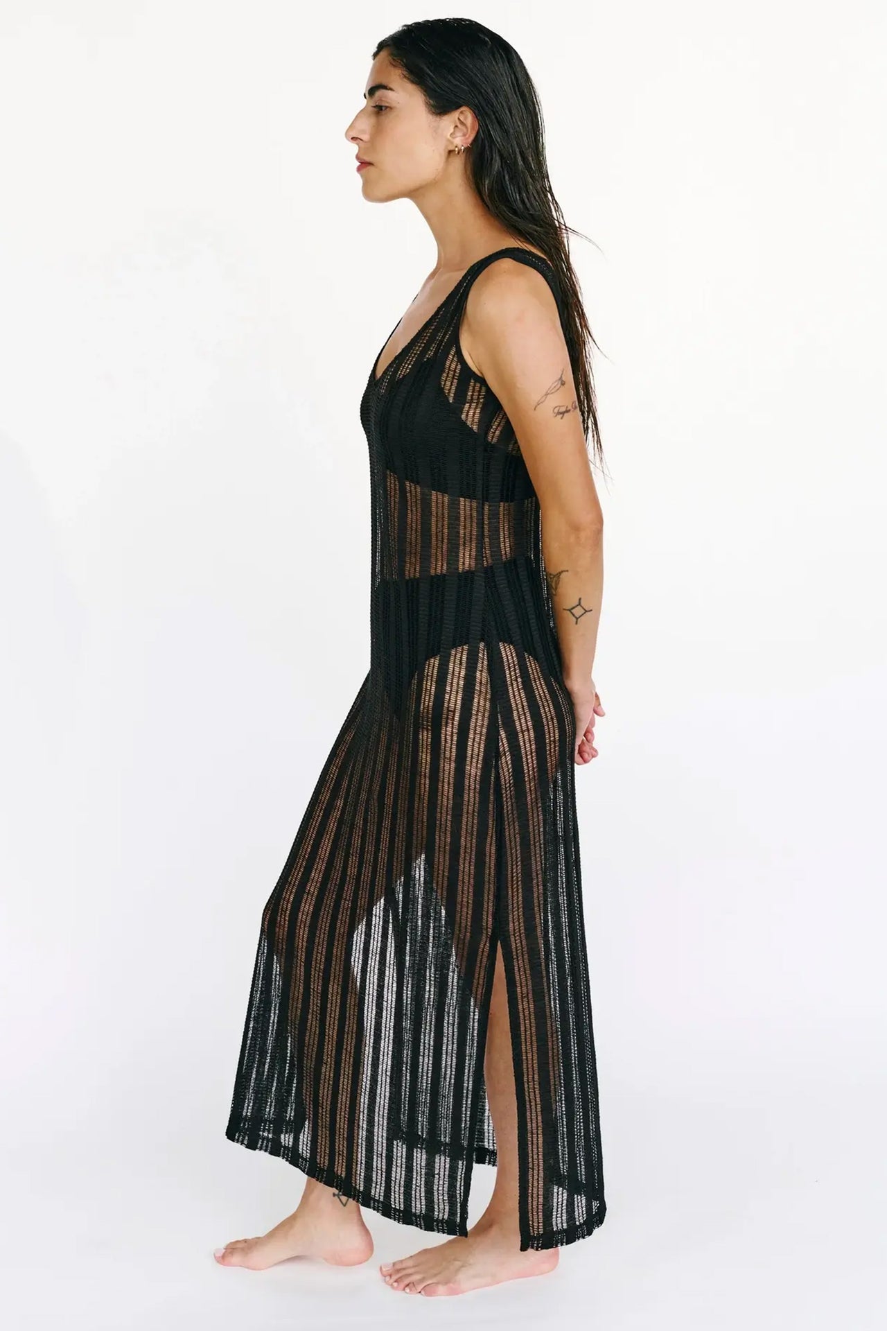 Else St. Tropez black knit swim coverup dress. The knit features a sheer striped pattern. The sleeveless dress has a scoop neck and side slits, with an ankle length hemline. Front view shown on model wearing a two piece black swimsuit underneath.