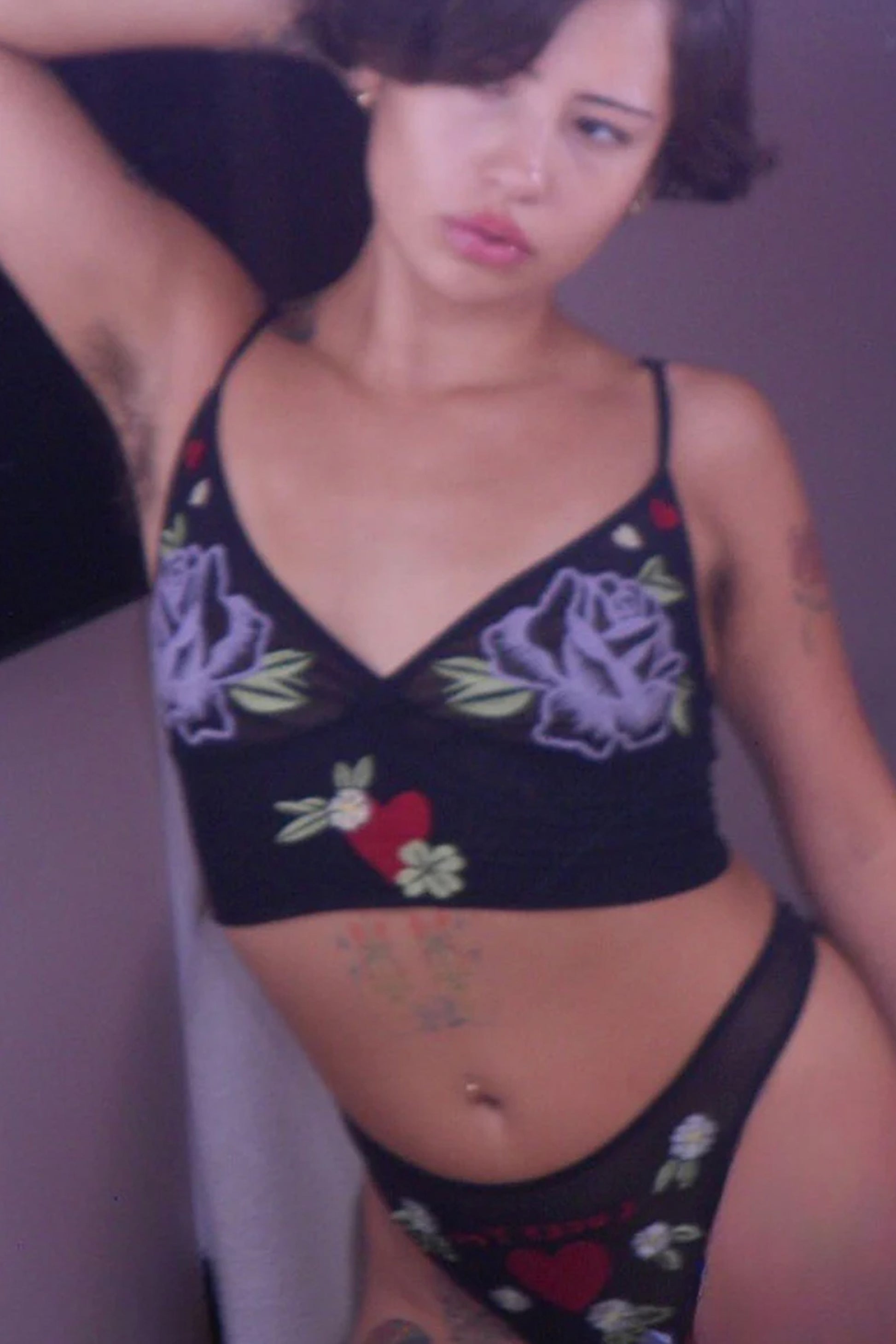 Only Hearts Aloha Honolulu Rosebud Cropped Camisole in sheer black mesh. Embroidered cups feature a purple rose with green leaves and red and white hearts. Longline band features a red heart with green and white florals surrounding it at center front. Shown on model in matching "lucky you" thong. Front view. 