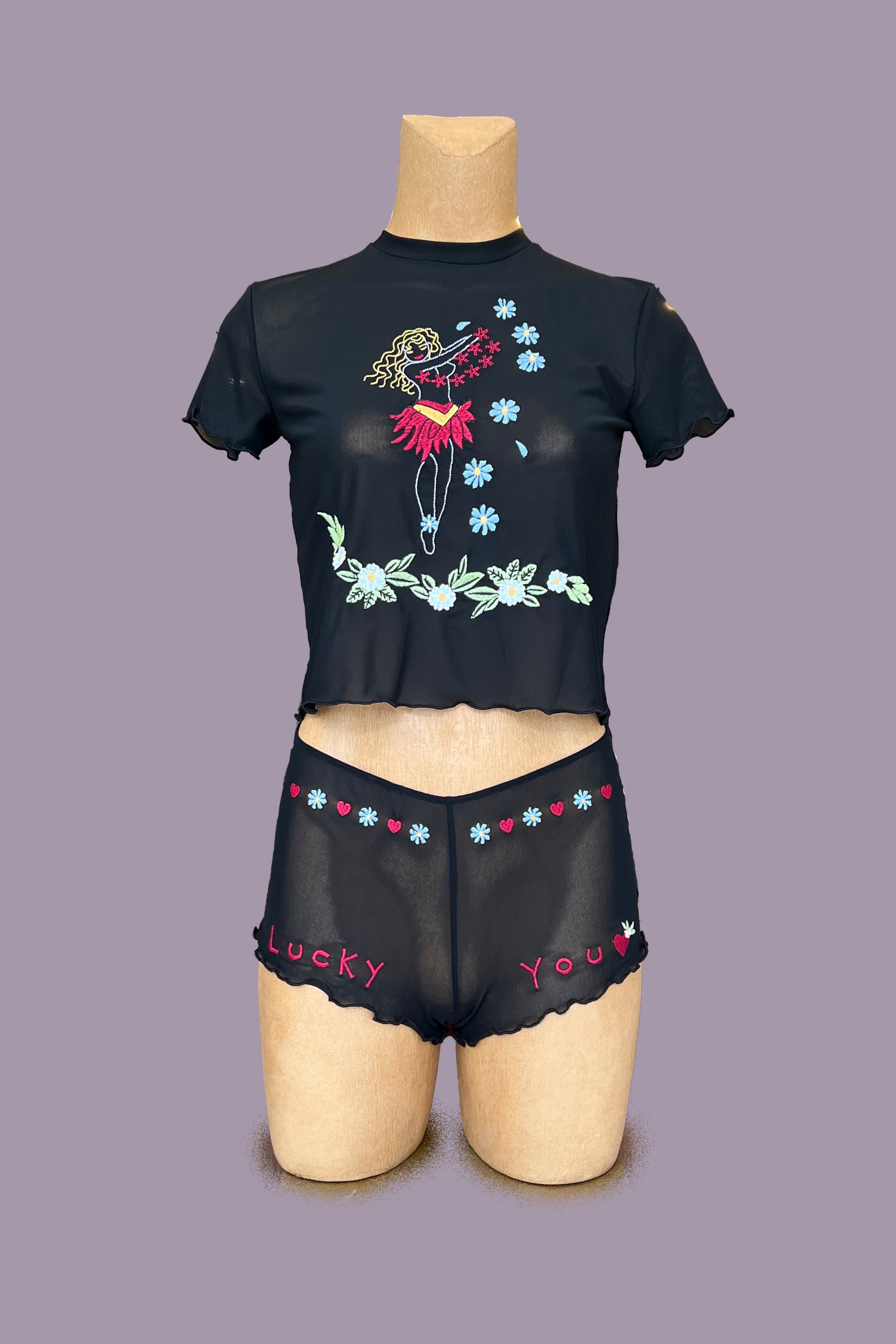 Only Hearts Aloha Honolulu Flower Girl Baby Tee in black mesh. Shown on mannequin, front view,showing lettuce edge on sleeves and hem, and floral and hula girl embroidery. Shown with matching embroidered boy shorts with "lucky you" and floral embroidery. 