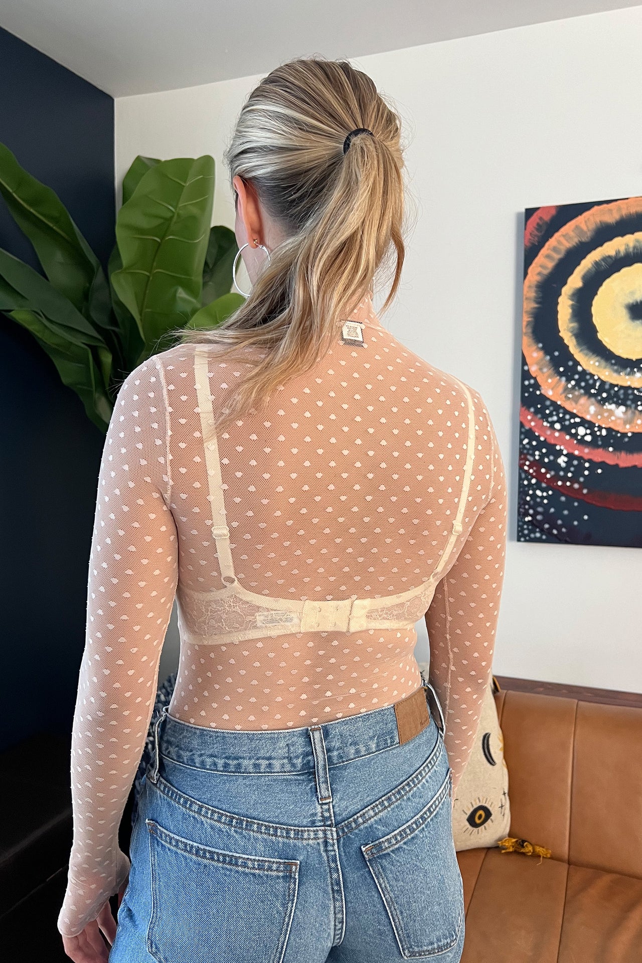 Only Hearts Coucou Lola mockneck long sleeve bodysuit in light pink beige polka dot mesh. Image hows bodysuit styled with ivory lace bralette underneath and light denim jeans and greige leather ankle boots. Thumb holes on bodysuit sleeves also visible. 