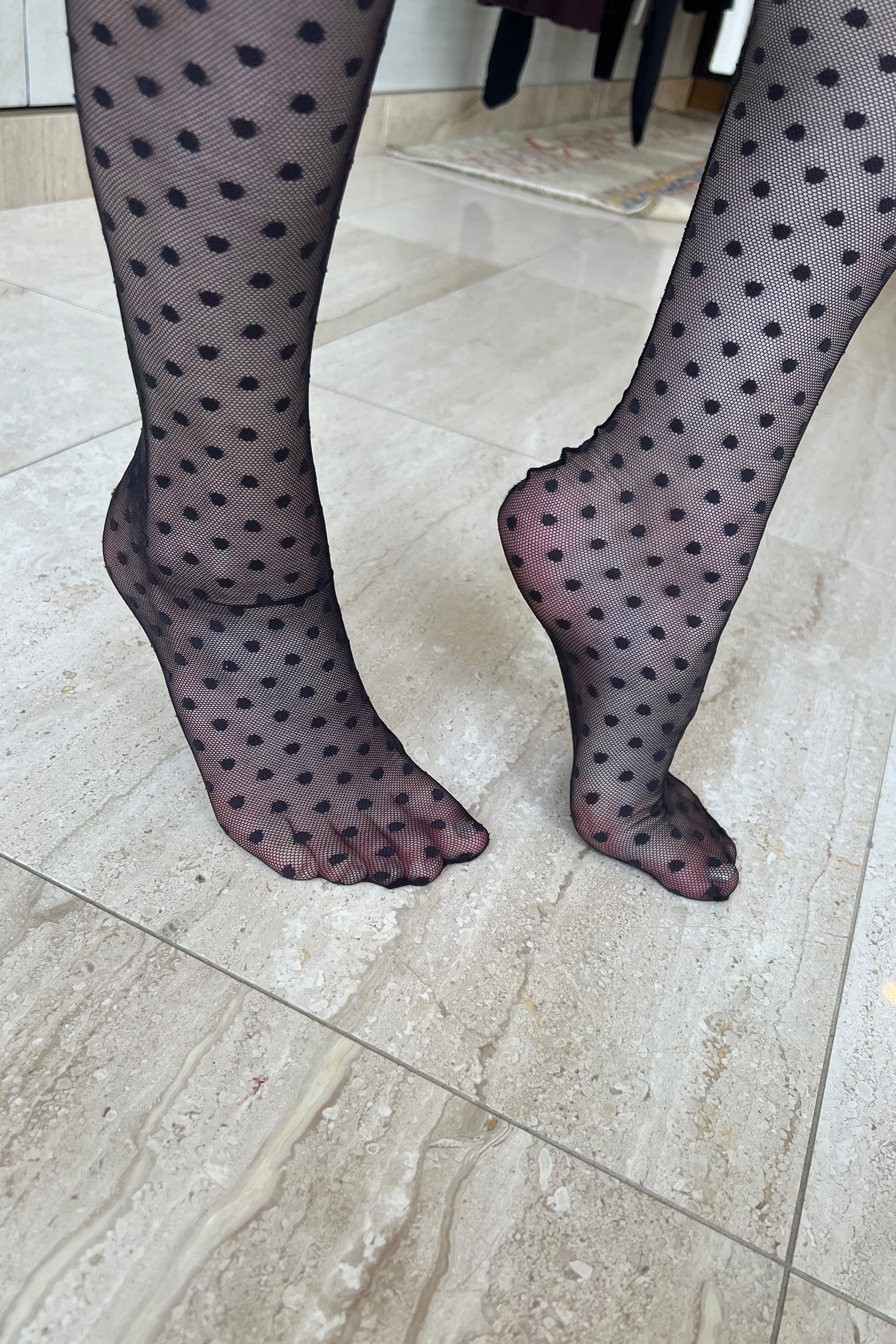 Only Hearts Coucou Lola ankle socks in black, front/side view on model. Image shows socks pulled up near the knee, polka dot mesh, and rolled edge top. Back seam is partially visible.  Model wears no shoes so fully sheer foot is shown.