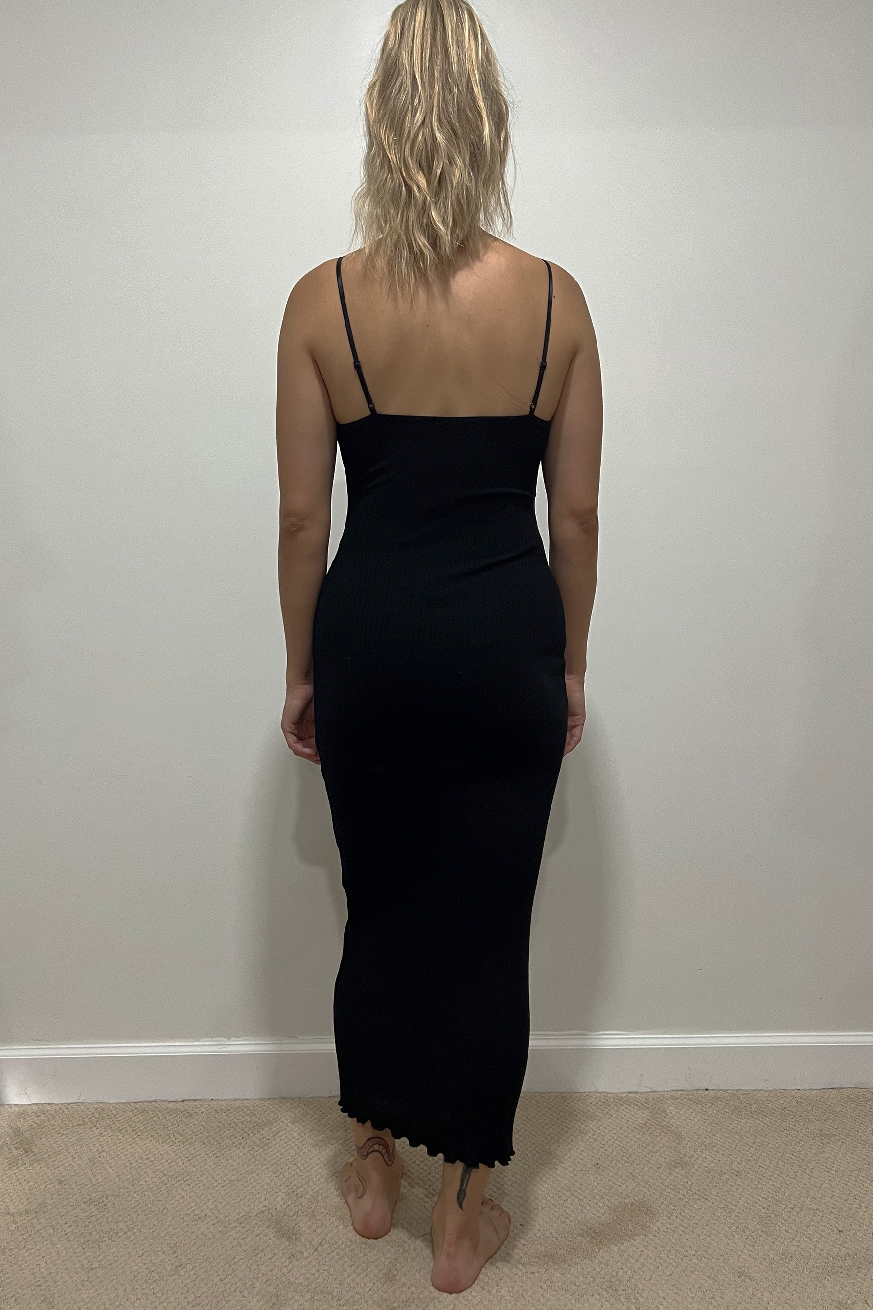 Only Hearts Eco Rib slip dress in black, back view on model. Image shows midi length lettuce edge hem, adjustable spaghetti straps, straight back, and clingy silhouette. 