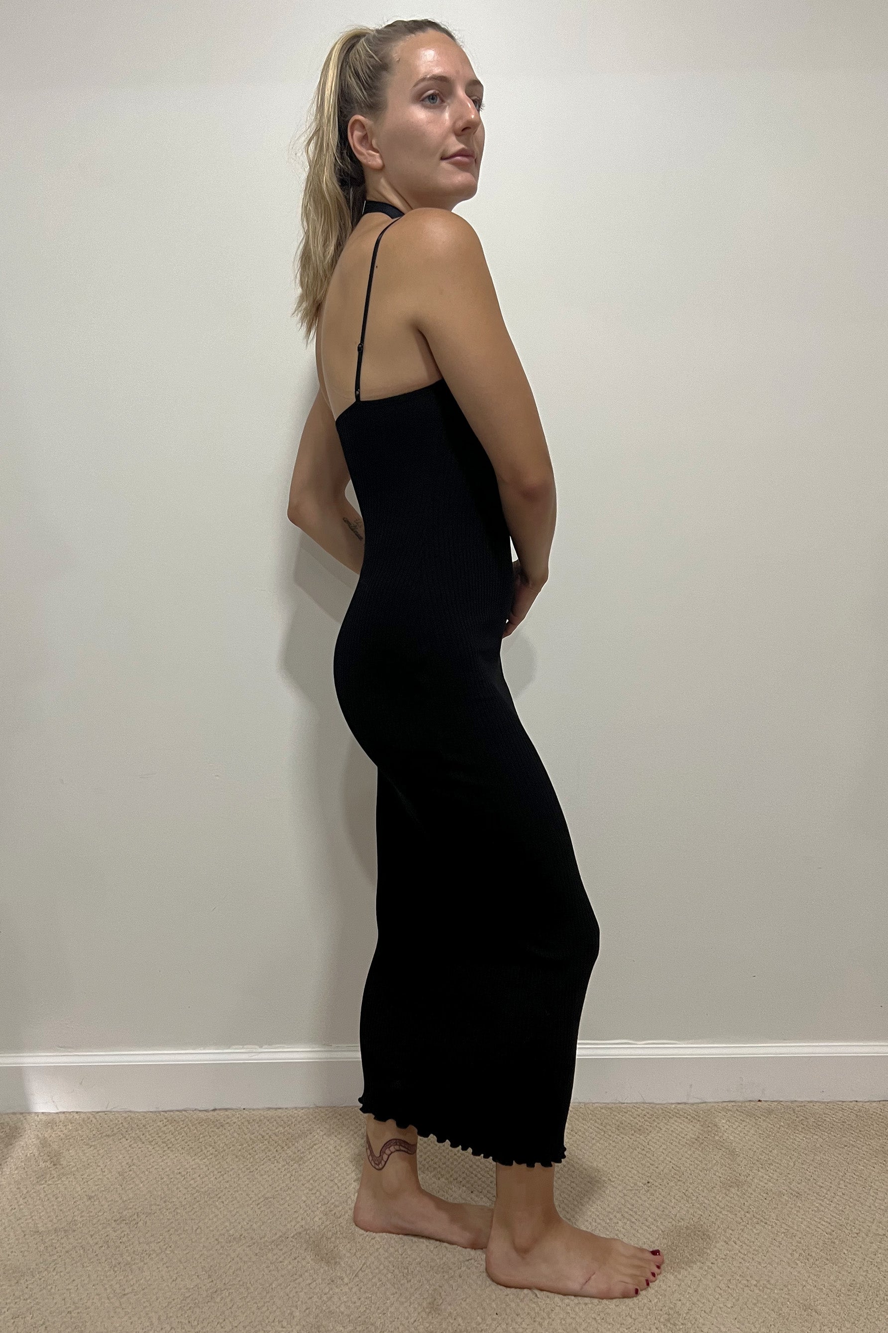 Only Hearts Eco Rib slip dress in black, side view on model. Image shows midi length lettuce edge hem, adjustable spaghetti straps,  and clingy silhouette. 