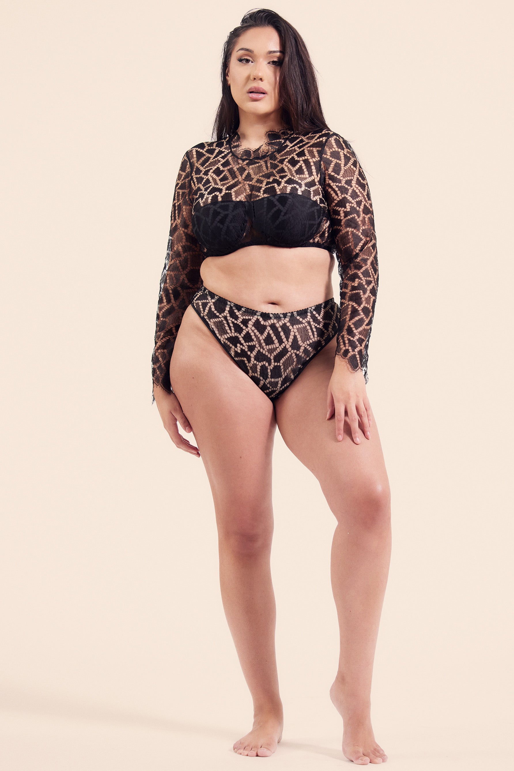 Paloma Casile Gilda Parisian high waist thong in black mosaic style lace. Front view on model in matching long sleeve crop top. Elastic waistband and leg trim. High cut leg and high rise waistband that dips a bit at the center just under the navel.