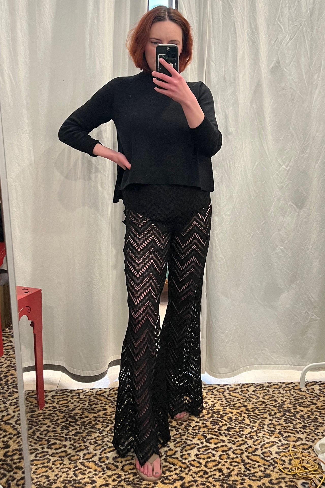 Paloma Casile Maxine black lace pants, shown on model, front view. Model is wearing matching lace halter style bralette. The pants have a black elastic waistband, built in opaque brief for modesty, and the sheer lace is a geometric chevron design with pointy angled hemline. 