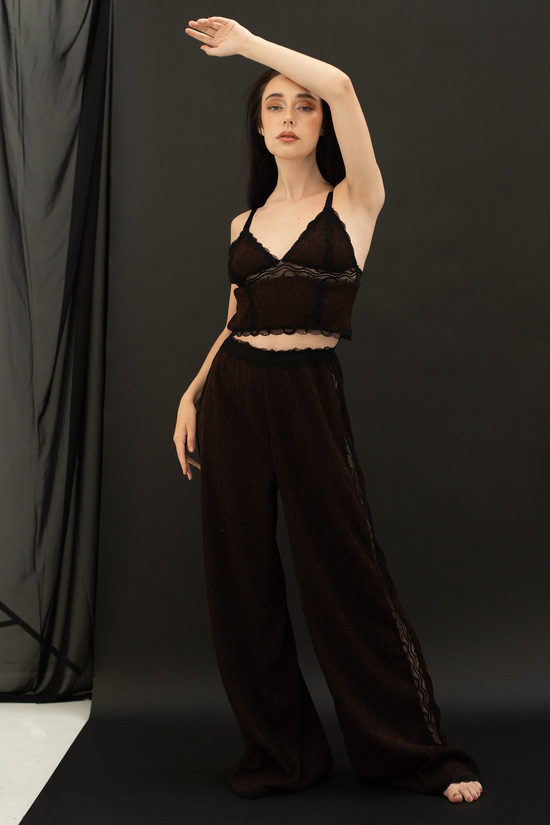 Paloma Casile La Nuit Rachel triangle cami top in dark chocolate brown and black lace, front view on model. Triangle cups with black lace trim and underband, black elastic shoulder straps and black lace trim at cropped hemline. Main fabric is brown crinkle finish. Shown with matching lounge pants. 