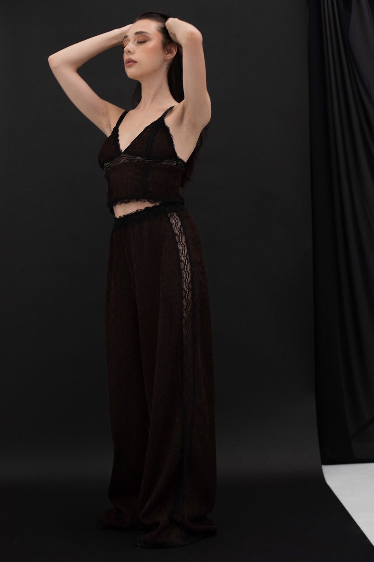 Paloma Casile La Nuit Rachel triangle cami top in dark chocolate brown and black lace, front view on model. Triangle cups with black lace trim and underband, black elastic shoulder straps and black lace trim at cropped hemline. Main fabric is brown crinkle finish. Shown with matching lounge pants. 