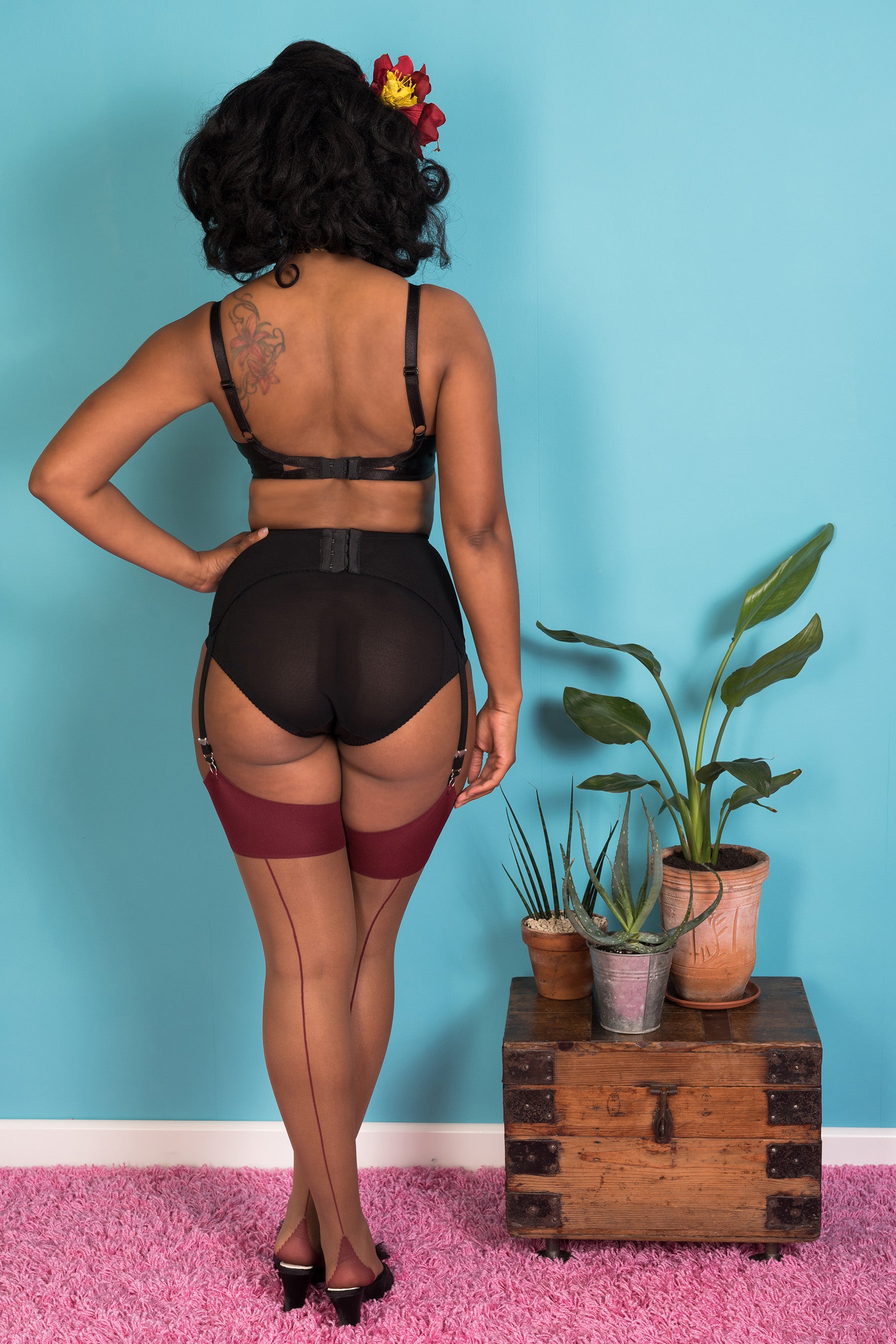 What Katie Did medium/dark nude and burgundy claret seamed stockings, back view shown on model. Image shows the wide claret welt, thin claret back seam and foot, and sheer nutmeg nude legs.